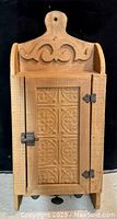 Front view of the wooden cabinet shaped like a cutting board with carved scrollwork and tin door with hinge and latch