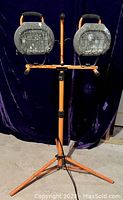 Front view of the HDX work lights on tripod, show two halogen lamps with metal cages and orange stand.