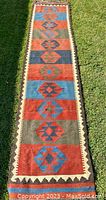 Full length view of the colorful geometric patterned kilim rug laid out on grass. Shows panelled diamond motifs and earth tone stripes.