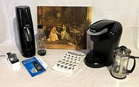 Overview of all items in the lot showing the Keurig coffee maker, SodaStream with bottle and manual, French press, electric sharpener, and canvas print.