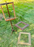 Wooden tripod easel holding one frame, two other wooden frames on grass