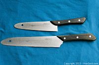 Pair of Mac chef knives laid flat showing full blades and handles on blue towel background
