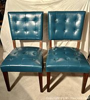 Front view of two teal padded and tufted vegan leather side chairs with hardwood angled legs.