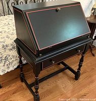 Full angular view of petite slant-top secretary desk showing black finish with red pinstriping and turned legs.