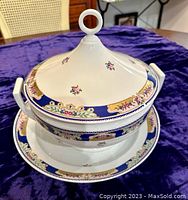 Overall angled view of covered tureen on matching platter showing the lid with loop handle and floral, blue, and gold border decoration.