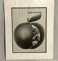 Full view of the matted and shrinkwrapped black and white Apple Records lithograph showing apple with imagery inside slice.