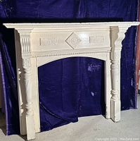 Full view of creamy glossy painted hardwood wooden mantle surround with carved tapered legs and decorative details