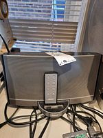 Full front view of Bose SoundDock speaker with remote placed in docking station on front of unit. Visible cables connected at the back.