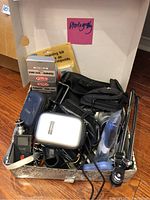 Photo showing various camera accessories including cleaning kit, cases, cables, and tools in a box