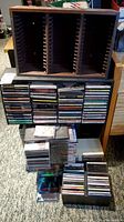Wooden CD storage rack with multiple stacked CDs in jewel cases, some stacked on the floor.