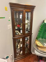 Full view of the tall wood corner curio cabinet with glass doors and multiple shelves inside