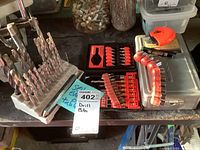 Overview photo showing assorted drill bits in a plastic stand, bit sets in red cases and a curved socket holder with chrome sockets.