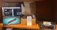 Photo showing Trendnet wireless network solution box, WD TV Live HD media player box, mini keyboard presenter combo box, and jeweler's visor magnifier on wooden shelf.