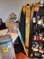View of the patio umbrellas in original tall boxes and the hammock with woven green rope and wooden spreaders leaning against wall.
