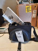 Sony camcorder and accessories inside black Sony carrying case with maxsold lot tag labelled 'Handycam'. Manual partially visible inside case.