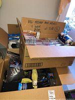 Three open cardboard boxes showing assorted men's socks and briefs. Socks include multiple pairs of white, grey, black, and other colors including packaged thermal socks by Tuffgear. Briefs are labeled as new Mossimo brand, size small.