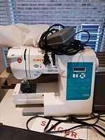 Front side view of sewing machine showing power cords and foot pedal on top.