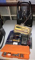 Photo showing assorted tool sets including drill and screwdriver bits, precision bit set in yellow case, digital multimeter, and orange organizer with screws and bits on the table in front of tool tote.