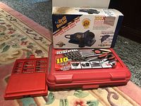 Red carrying case labeled Ultra Steel 110 piece tool set set beside boxed Drill Doctor bit sharpener and smaller red case of driver bits on carpeted floor.