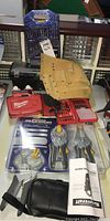 Photo showing the collection of tools including Lockjaw clamps, tool belt, Milwaukee Shockwave bit sets, drill and screwdriver bit sets, spring clamps, and Mastercraft digital clamp multimeter pouch and manual.