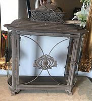 Front and side view of a rectangular wrought iron lantern with glass panels and decorative ironwork detailing, showing some rust and spots on metal surface.