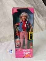 Front view of 1997 Coca Cola Picnic Fun Barbie doll in original packaging showing the doll dressed in red top, denim vest and checkered pants with Coca Cola picnic accessories.
