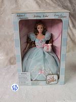Front view of Barbie doll in original Birthday Wishes 2000 box, showing doll in blue dress holding gift box.