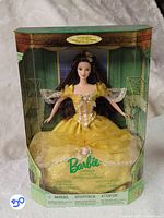 Front view of Barbie Belle doll in original box showing yellow dress and packaging artwork.