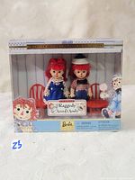 Front view of unopened Raggedy Ann and Andy collector dolls in box showing dolls and small red chair