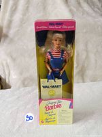Photo of front view of Barbie doll in original yellow Walmart box showing the doll in blue overall skirt and striped shirt.