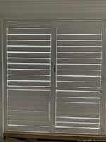 Front view of closed white California shutter panels with horizontal slats and central latch.