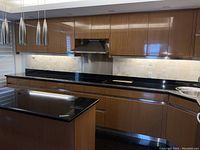 Linear arrangement of upper and lower lacquered bamboo cabinets with black granite countertop and central range hood cutout
