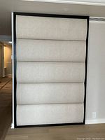 Front view of the large rectangular padded panel with tan segments and black frame leaning against a wall indoors next to an air vent.