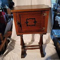 Front view of the 1920s-30s wooden smoking cabinet with door closed. Shows decorative cutout in door and brass hinges.