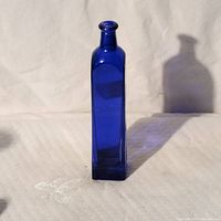 Front view of a tall cobalt blue glass bottle with square base and narrow neck