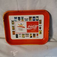 Front view of metal tray with orange border, white central panel, Barcelona 1992 Olympic logo, Coca-Cola logo, and images of Olympic posters.