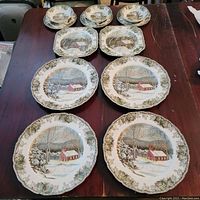 Set of Johnson Bros dinnerware on table showing four large dinner plates, two square salad plates, three sauce bowls, and three bread and butter plates with winter-themed scenic patterns.