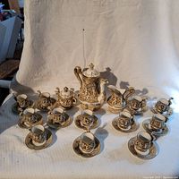 Full tea set displayed including teapot, creamer, sugar bowl, cups, and saucers on white cloth backdrop.