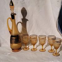 Full view of Bohemia crystal decanter with ground glass stopper and five matching glasses in frosted smoke brown with gold trims on white background.