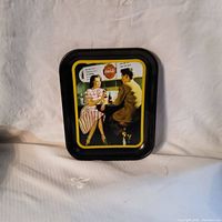 Front view of the vintage Coca-Cola metal serving tray showing a retro illustration of a man and woman sharing Coca-Cola bottles with speech bubbles and colored border.