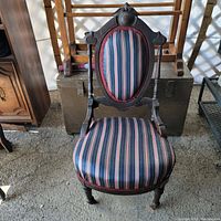Photo showing full view of Victorian parlor chair made of carved walnut with striped fabric upholstery.