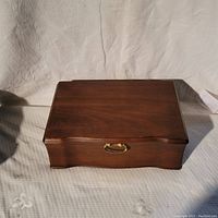Closed view of a dark wooden jewelry box with a brass handle.