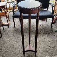 Full view of the vintage carved wood pedestal stand, showing three legs, round top, and the triangular base.