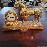 Full view of the vintage brass tone metal horse and the yellowish marble patterned base with a connected clock on the left side.