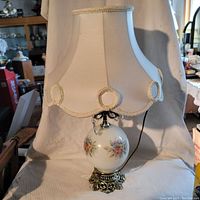 Full view of the vintage lamp with white fabric shade and floral painted glass globe on cast metal base