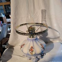Front view showing the entire lamp with glass chimney and floral decorated melon-shaped ceramic base