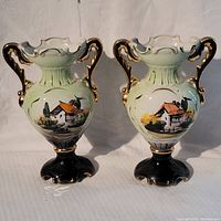 Pair of vintage porcelain vases with hand-painted scenic cottage artwork and gold accents on handles and base.