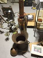 Antique brass fire extinguisher and round copper pot viewed from top with label tags visible; part of a basement setting.