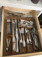 Top view of the drawer showing an organized wooden tray with several compartments containing forks, knives, spoons, small forks, small spoons, and some serving utensils.