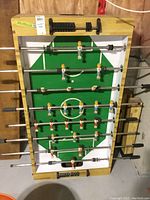 Full photo of vintage wooden foosball table with green field markings and plastic player figures on rods.